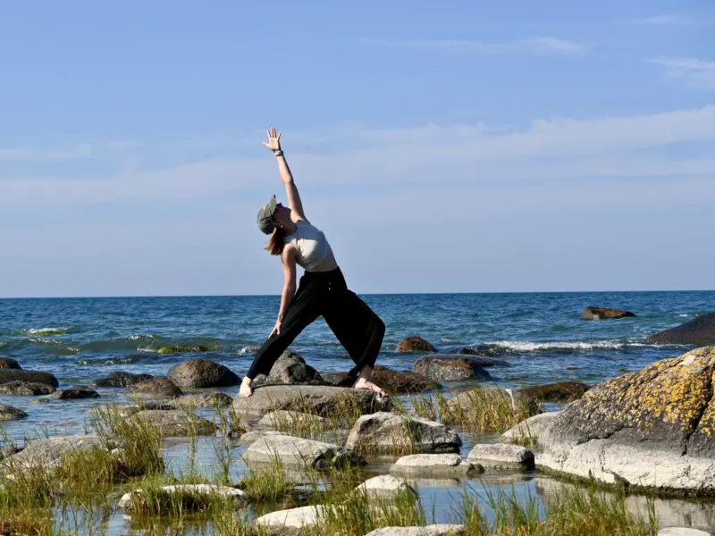 Sara Felsberg übt eine kraftvolle Yoga-Pose auf Felsen am Meer