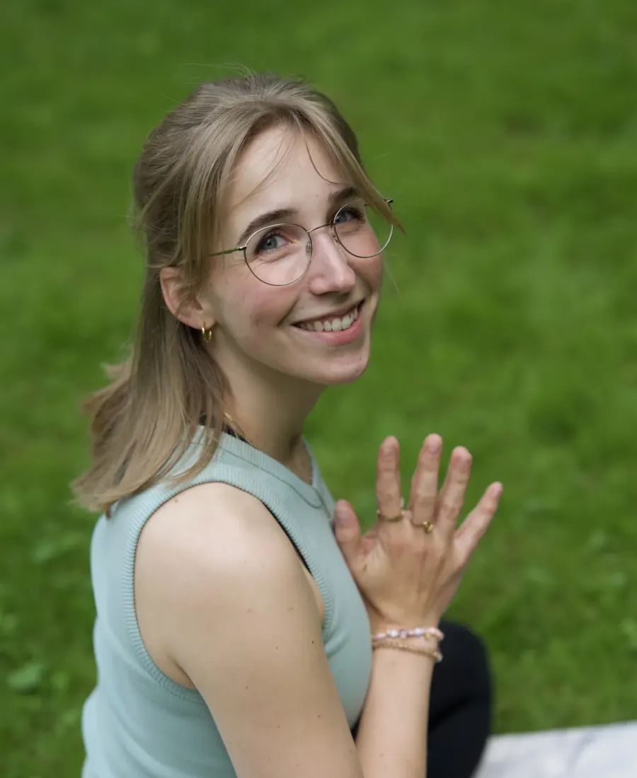 Sara Felsberg sitzt lächelnd auf einer Yogamatte im Grünen